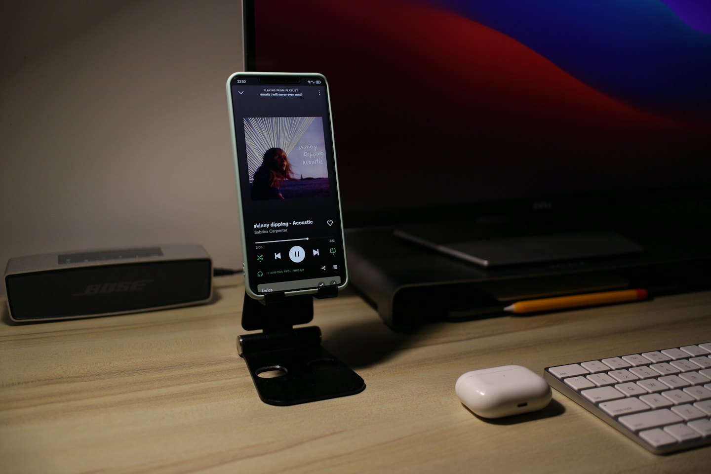Smartphone playing music on a wooden desk with electronic accessories.