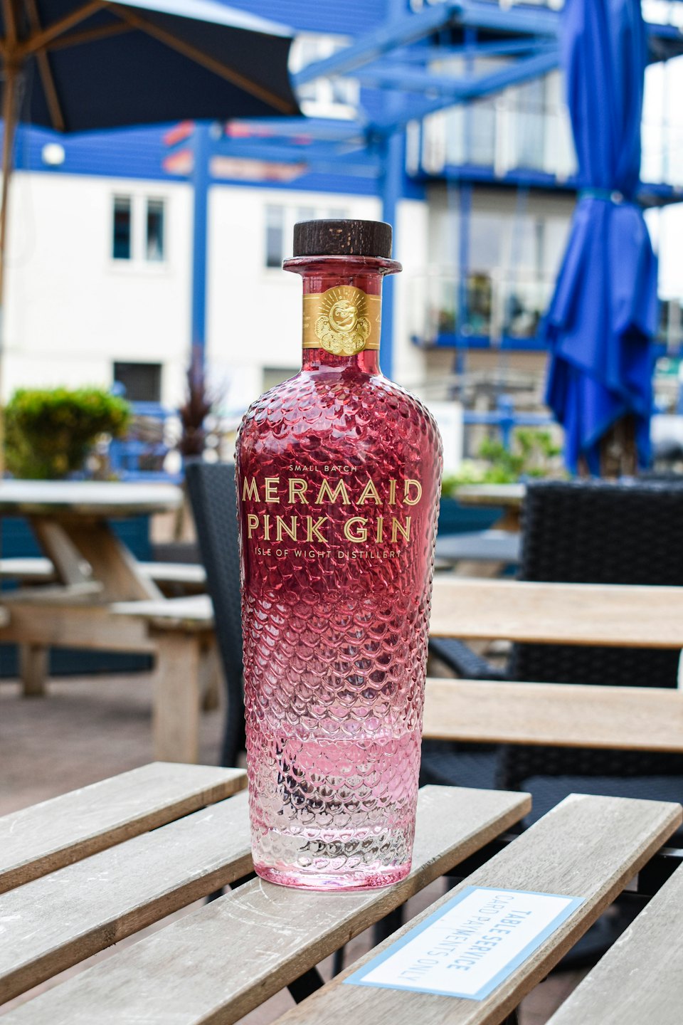 A bottle of Mermaid Pink Gin sits on a wooden table.