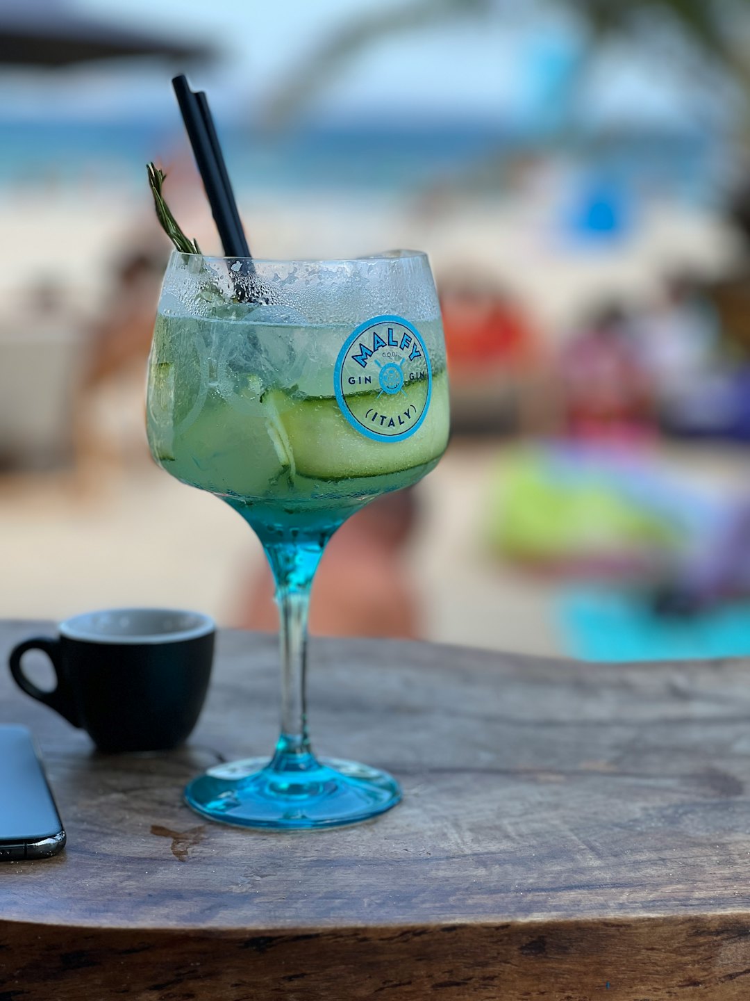 A gin and tonic with cucumber and rosemary on a wooden table.