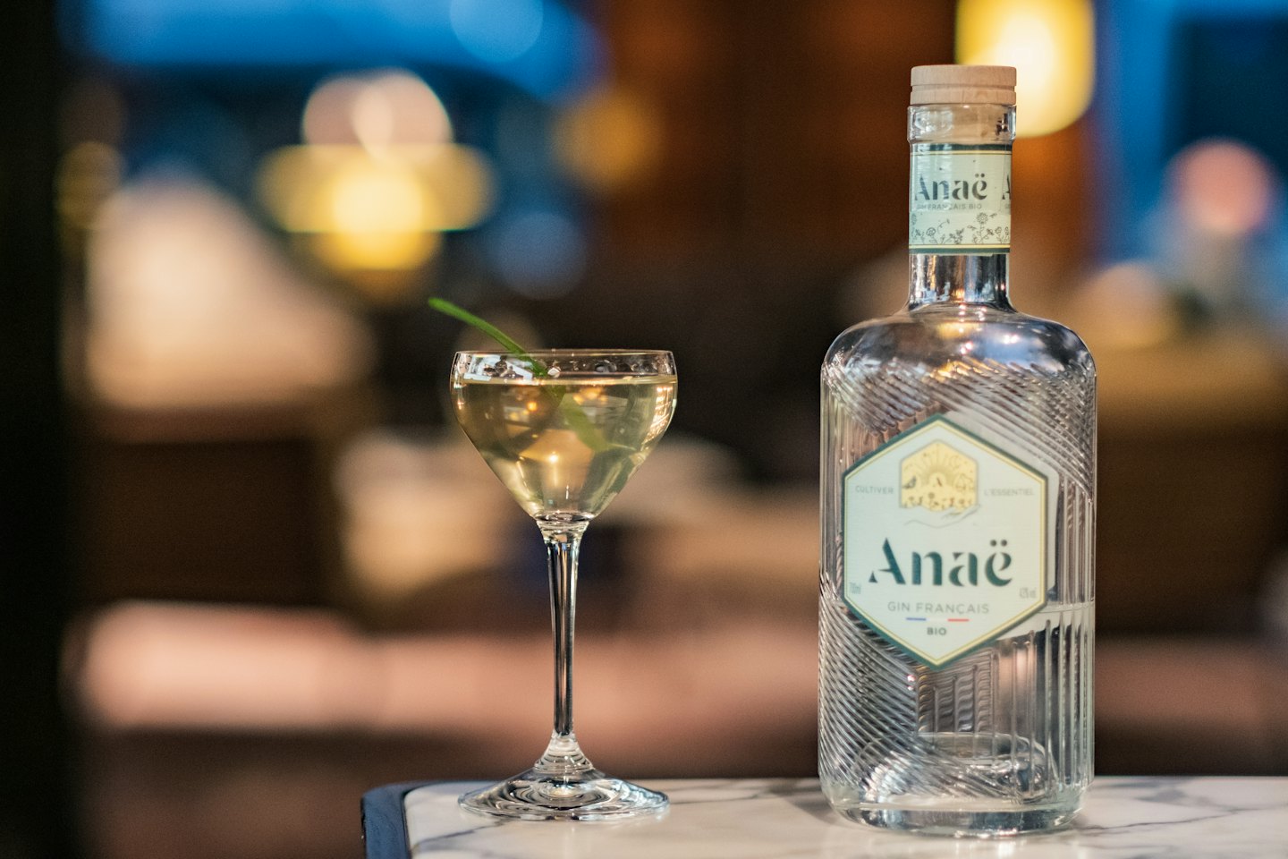 A glass gin bottle and cocktail sit on a marble surface.