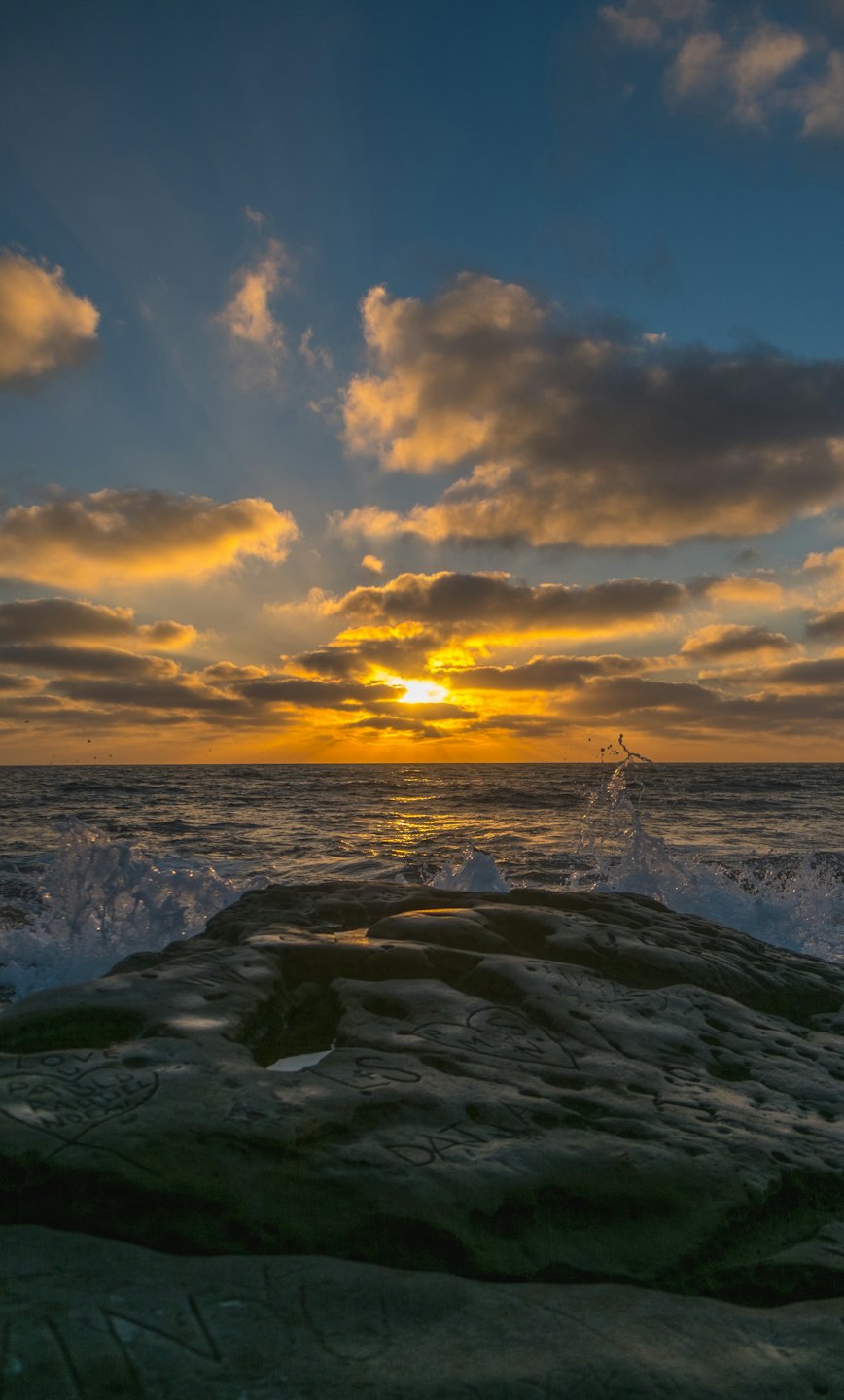 Golden sunset over crashing ocean waves near rocky formations.