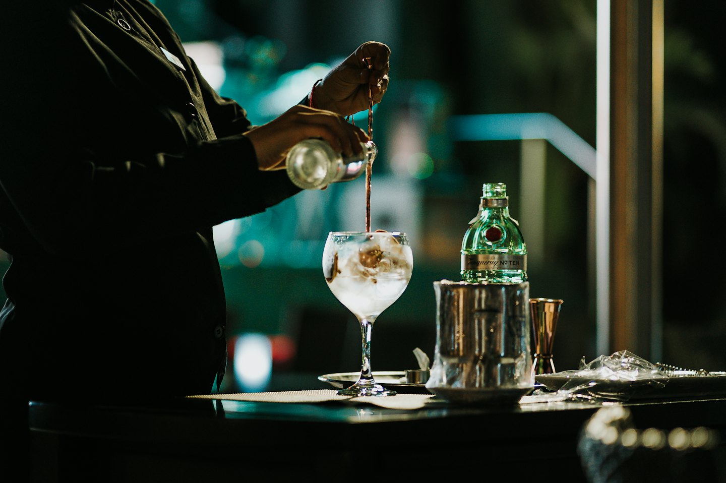Bartender pouring gin into a glass filled with ice.
